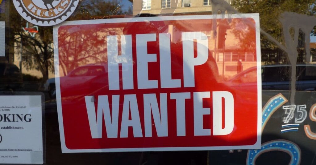 Placa de "procura-se ajuda", representando mercado de trabalho nos EUA em meio a cortes de empregos