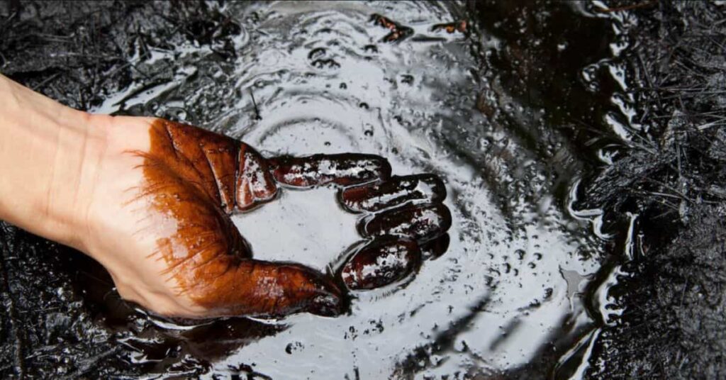 Mão coberta por petróleo bruto simboliza o preço do petróleo hoje em alta com risco no Estreito de Ormuz.