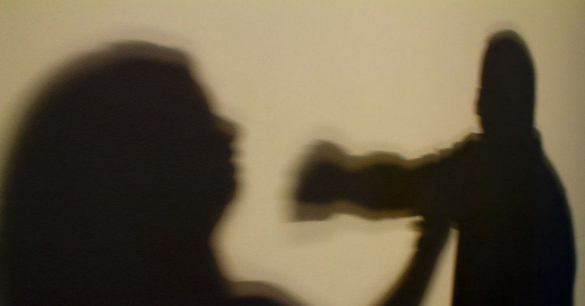ombra de agressor levantando a mão contra mulher em cena que representa violência doméstica