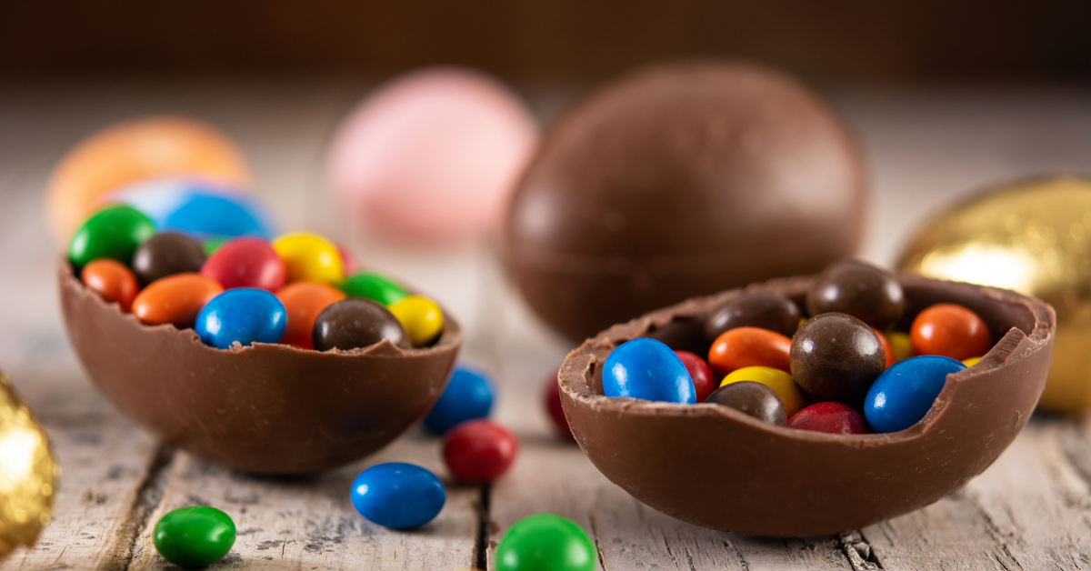 Ovos de Páscoa de chocolate recheados com confeitos coloridos sobre mesa de madeira - Foto: Freepik