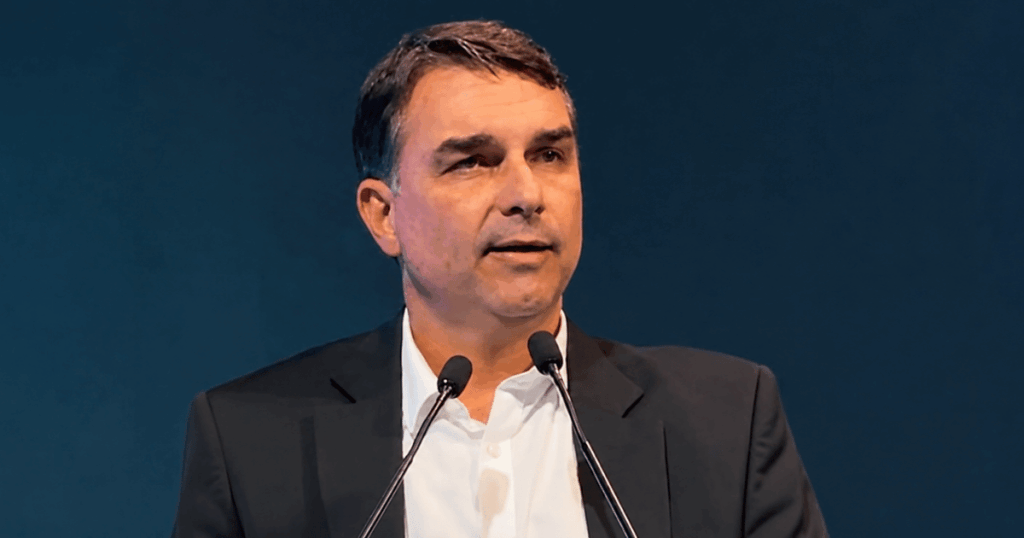 Flávio Bolsonaro durante discurso em evento político, imagem utilizada em reportagem sobre análise do Financial Times da crise com Michelle Bolsonaro.