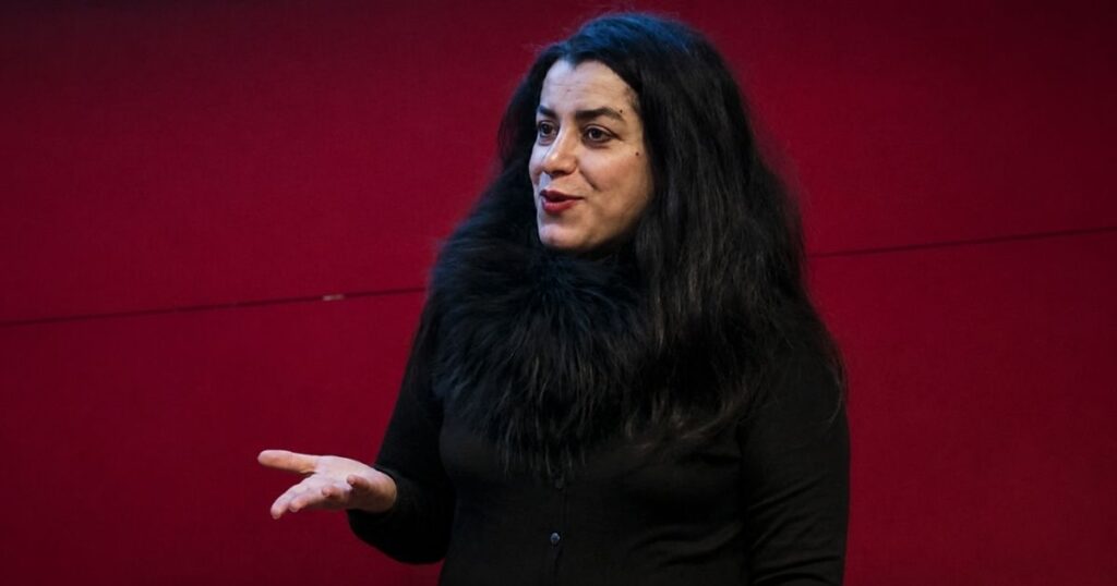 Marjane Satrapi durante evento público diante de fundo vermelho. A autora de Persépolis morreu aos 56 anos e deixou um legado global sobre o Irã, exílio e liberdade.
