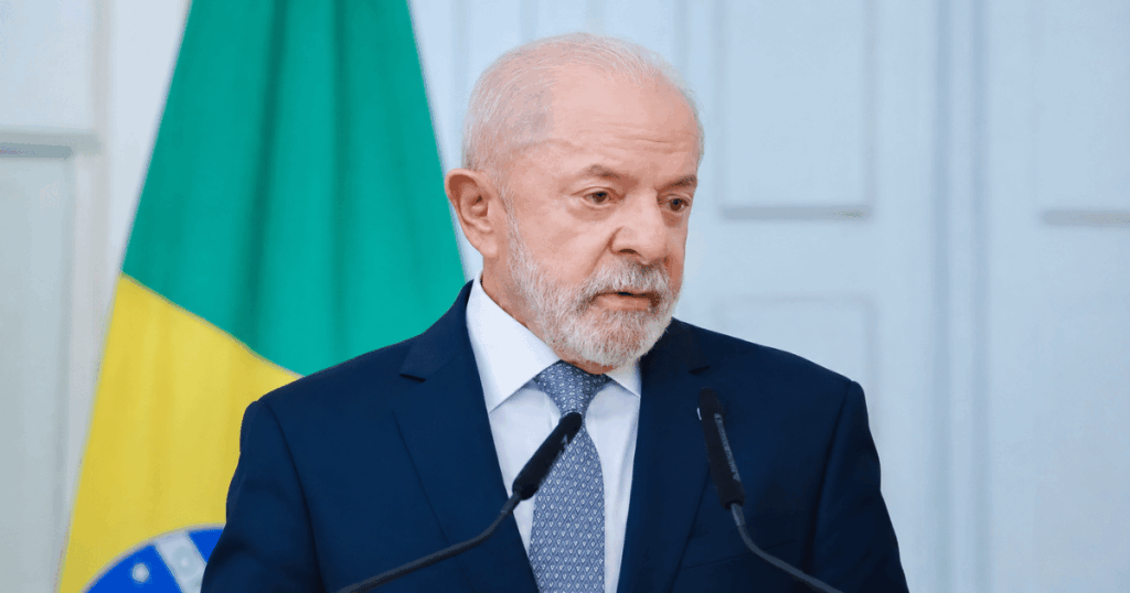 Autoridade governamental durante pronunciamento oficial em ambiente institucional com bandeira do Brasil ao fundo.