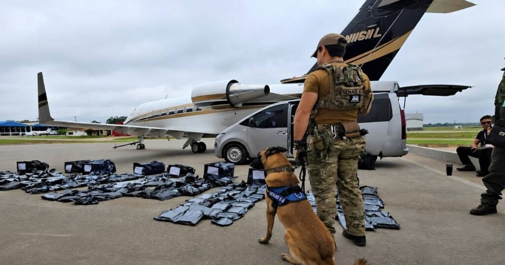 Agente da SENAD com cão farejador ao lado de jato executivo apreendido no Paraguai durante operação que encontrou 261 quilos de maconha premium.