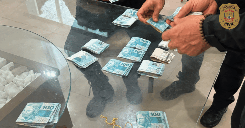 Agentes da Polícia Civil do Distrito Federal contabilizam cédulas de R$ 100 apreendidas durante uma operação policial sobre uma mesa de vidro.