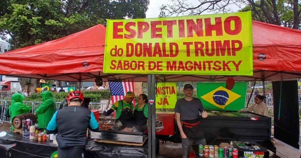 Barraca com placa “Espetinho do Donald Trump, sabor de Magnitsky” durante ato político em Belo Horizonte.