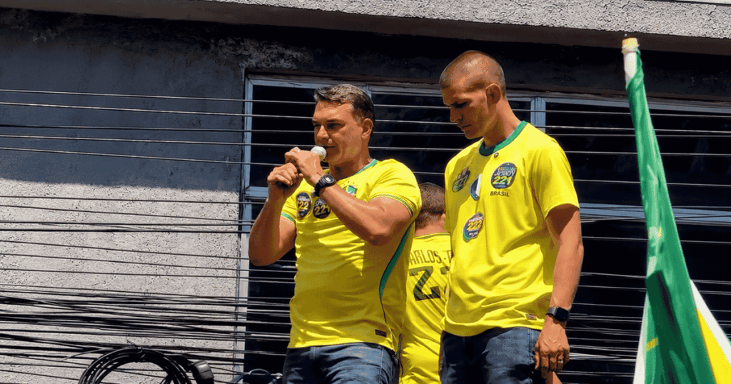 Flávio Bolsonaro fala ao microfone durante evento de campanha em São João de Meriti, na Baixada Fluminense.