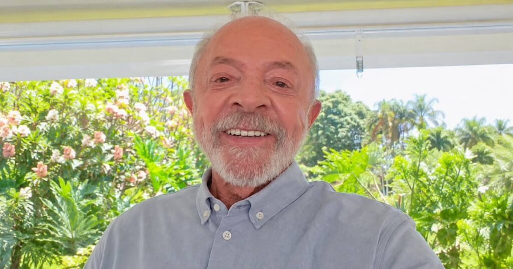 Presidente Luiz Inácio Lula da Silva aparece sorrindo, usando camisa azul-clara, em vídeo de convocação para a live com André Janones.
