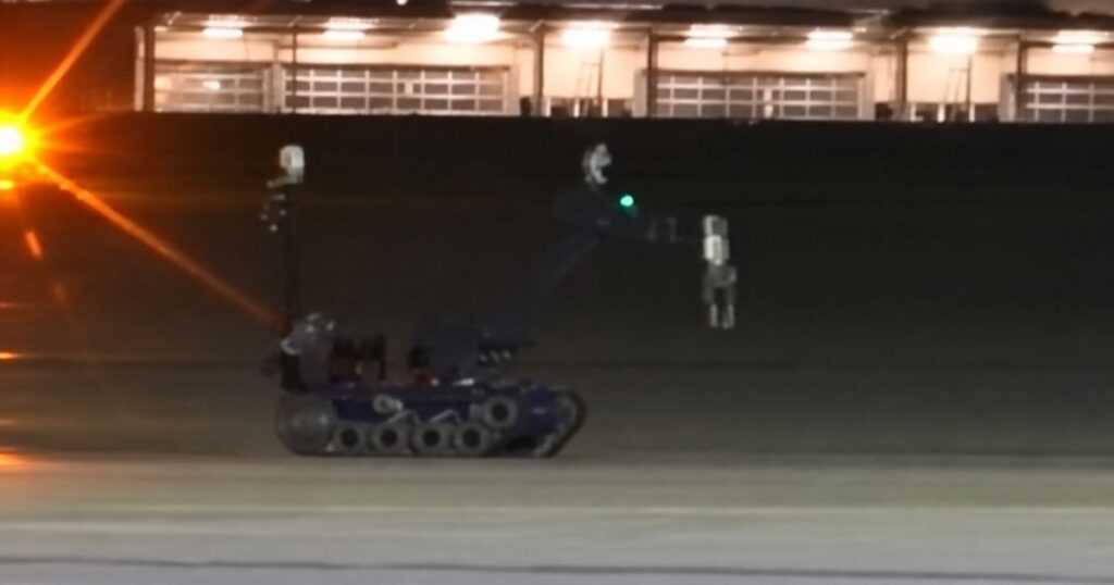 Robô sobre esteiras em área aeroportuária à noite, com instalações iluminadas ao fundo.
